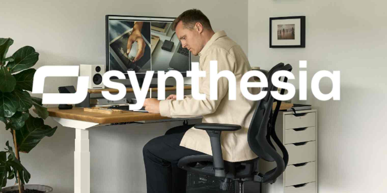 A man in a cream shirt works at a desk with the Synthesia logo layered over him.