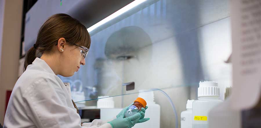 Scientist looking at a small glass jar with liquid