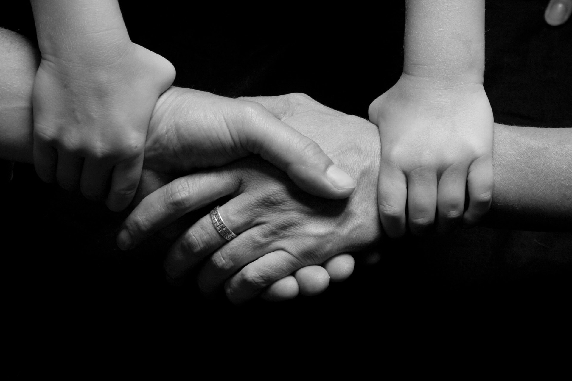 A black and white image of two hands shaking and at each wrist another hand grabbing the hands. 