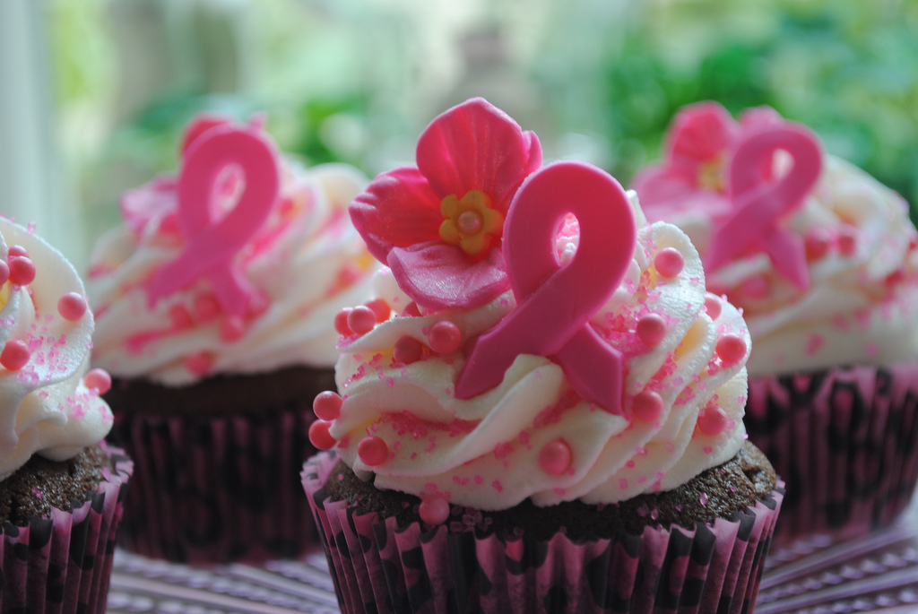 Cupcakes with white frosting and a pink sprinkles with a pink ribbon.