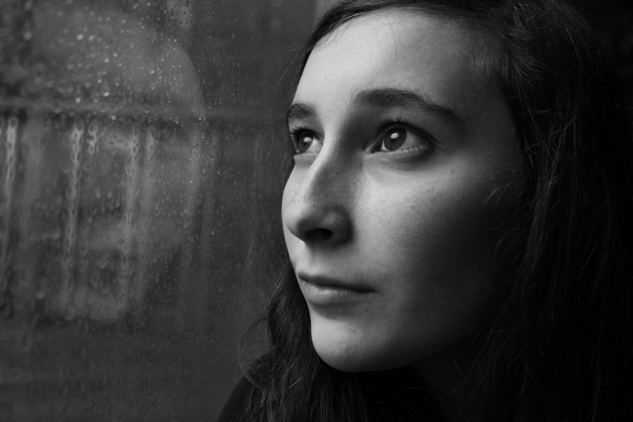 A black and white image of a woman looking up through glass that reflects her image. 