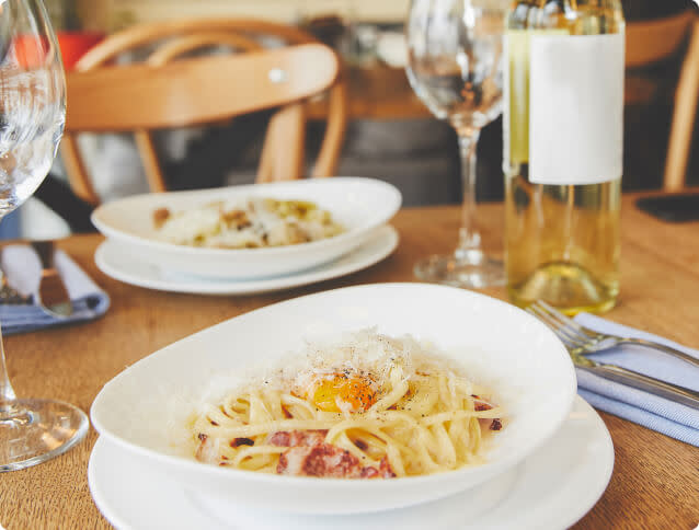 Two bowls of spaghetti carbonara on a table next to a bottle of Chardonnay wine and two glasses