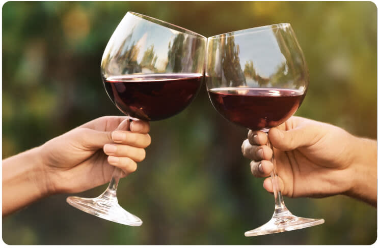 Two hands holding glasses of red wine toasting