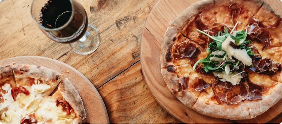 A glass of Merlot red wine on a table next to two pizzas