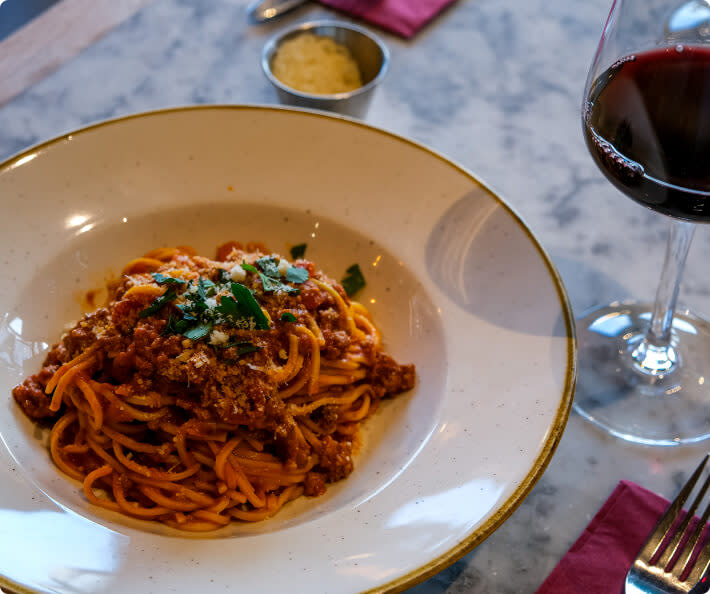 A plate of spaghetti with red bolognese meat sauce or ragu, next to a glass of red Chianti wine