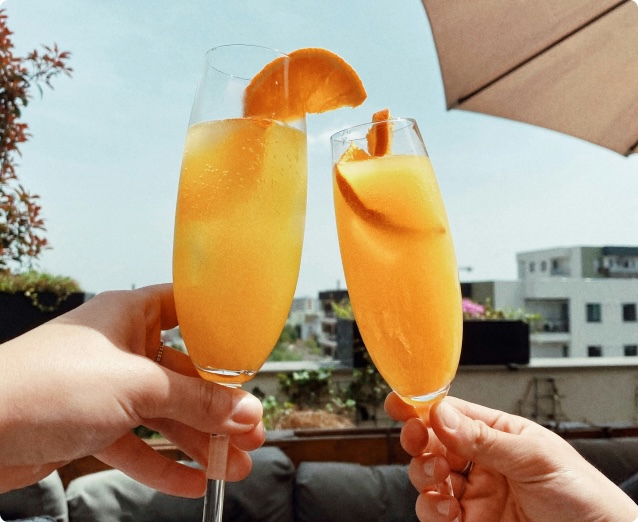 Two hands holding flute glasses of mimosa drinks