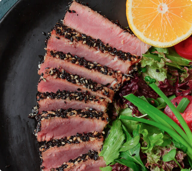Slices of seared sesame-crusted tuna steak on a plate with salad and an orange slice