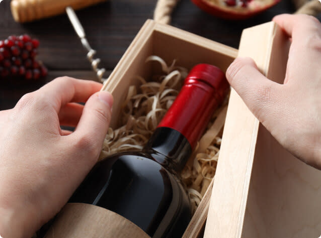 Hands opening a wooden box containing a bottle of red wine