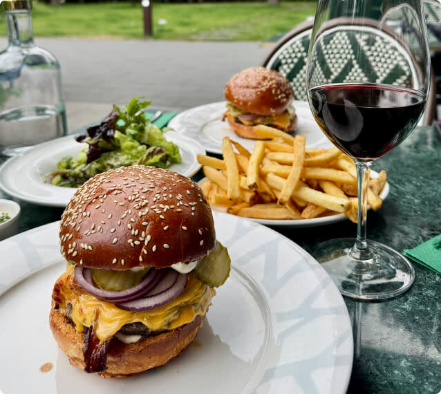 Hamburgers, french fries, and salad on plates next to a glass of red wine