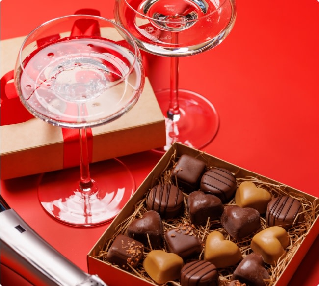 Glasses of white wine next to a box of Valentine's Day themed chocolates