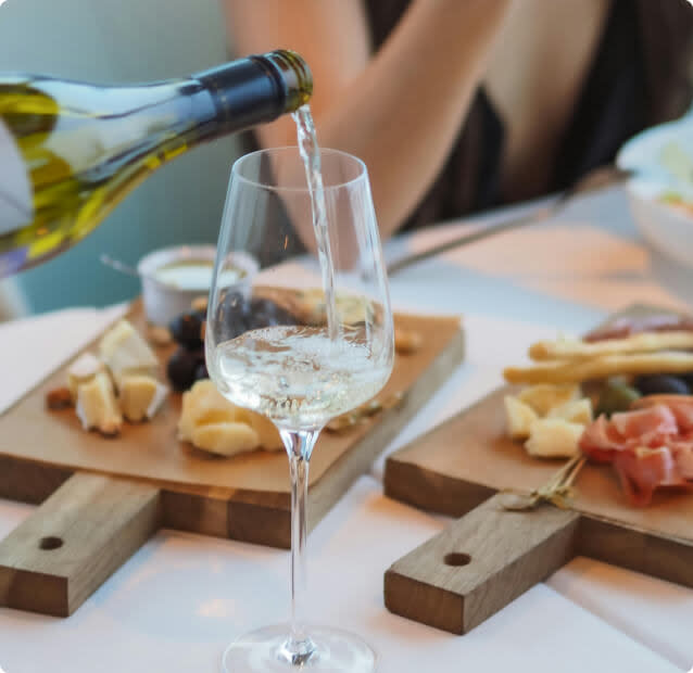 pouring a glass of Chardonnay wine into a glass with cheese and charcuterie in the background