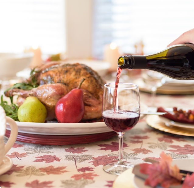 Pouring a glass of red wine to pair with a Thanksgiving roast turkey dinner