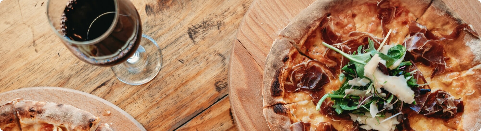 A glass of Merlot red wine on a table next to two pizzas