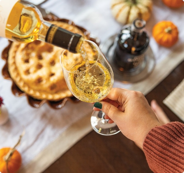Hand holding a wine glass while someone pours white wine into it. Thanksgiving table setting