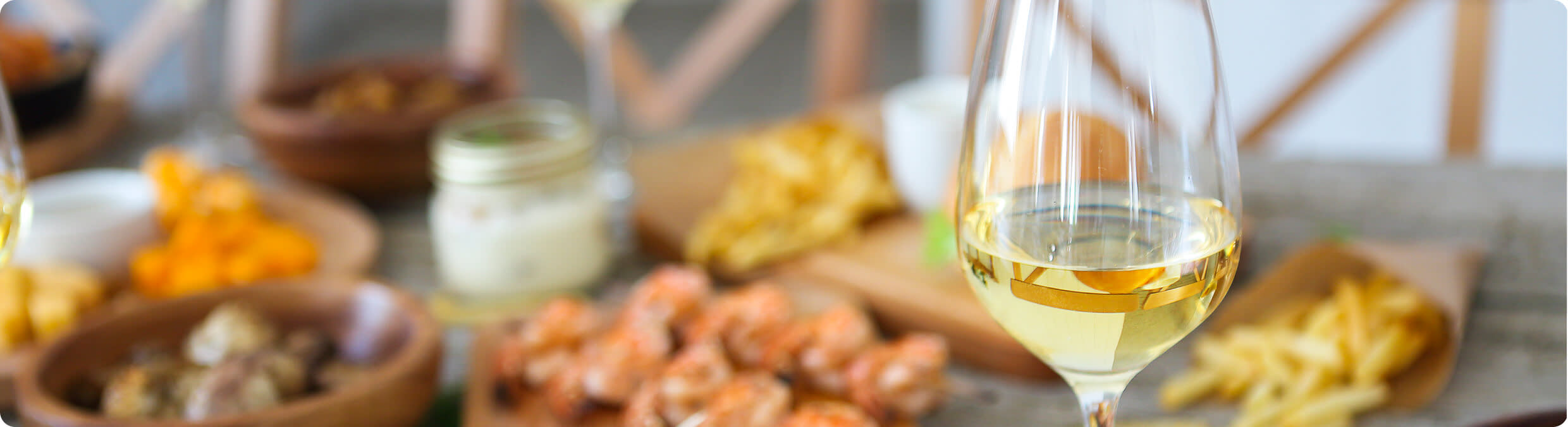 A glass of white Pinot Grigio wine with an array of dinner food in the background