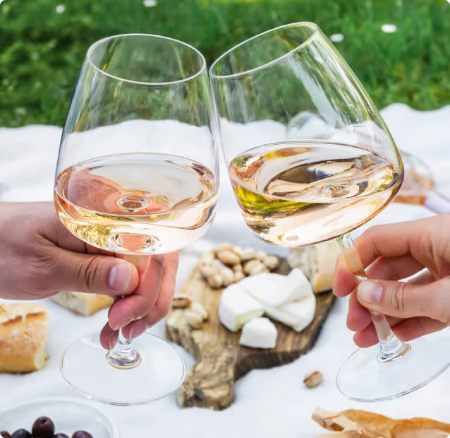 Two glasses of rosé wine toasting above a picnic blanket with cheese and other snacks