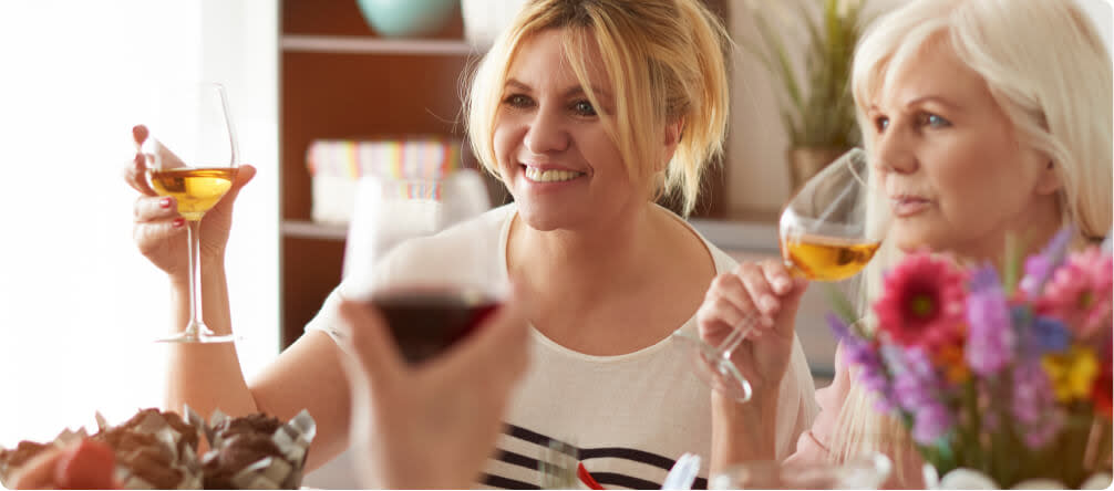 A photo of two women, one middle aged and one older, drinking wine and celebrating Mother's Day with flowers in the foreground