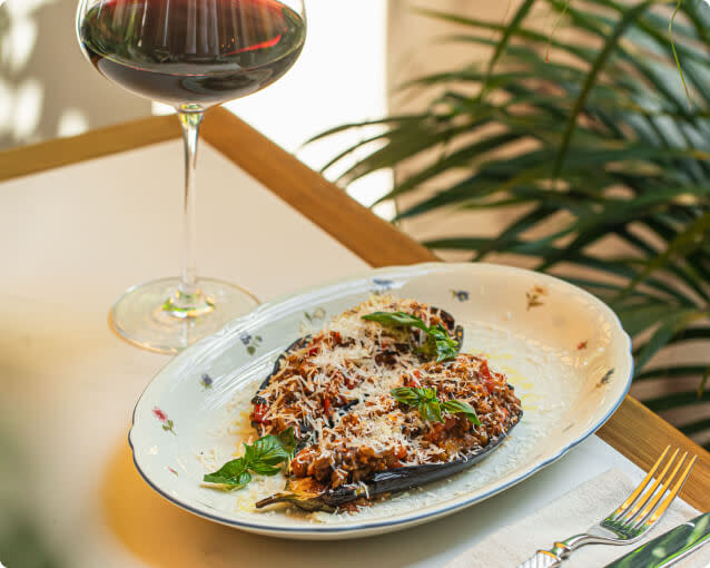 Eggplant parmesan on a dish next to a glass of red Merlot wine