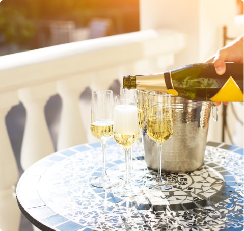 Hand pouring sparkling wine into flutes on outdoor mosaic table
