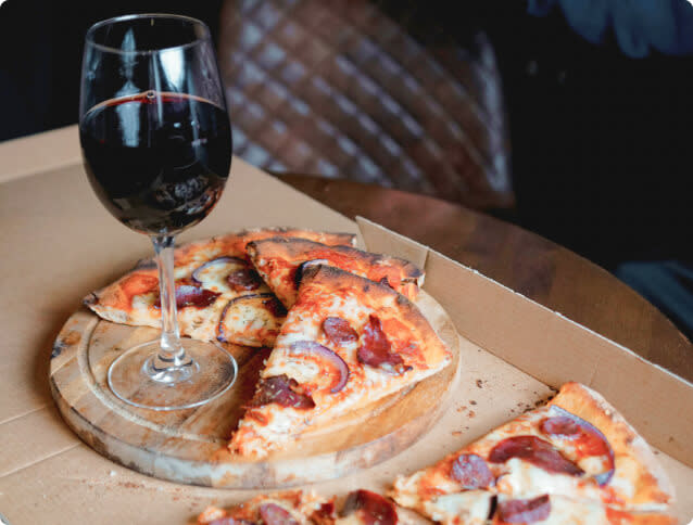 Slices of pizza and a glass of red wine in a cardboard pizza box