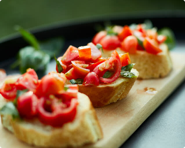 Three slices of tomato bruschetta toast with basil on a wooden cutting board
