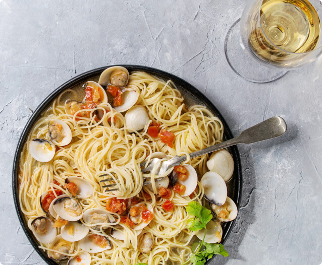 A large plate of pasta with clams and seafood paired with a glass of Pinot Grigio wine