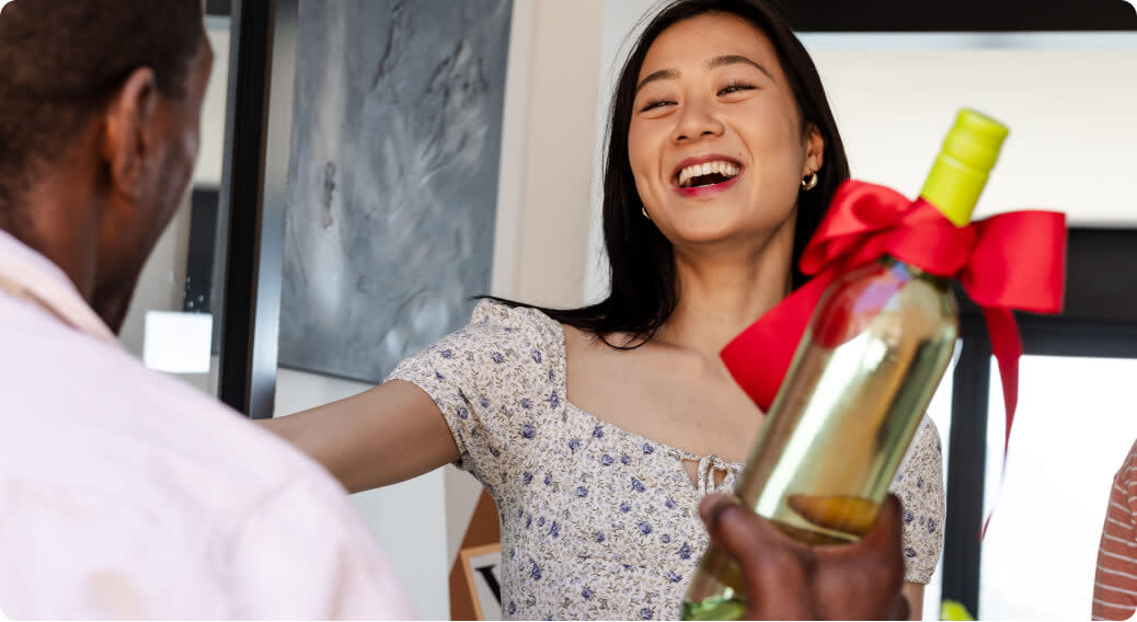 A woman happily receiving a bottle of wine as a gift from a man
