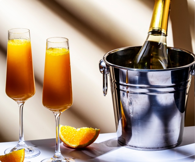 Two mimosa glasses next to an ice bucket containing a bottle of sparkling wine