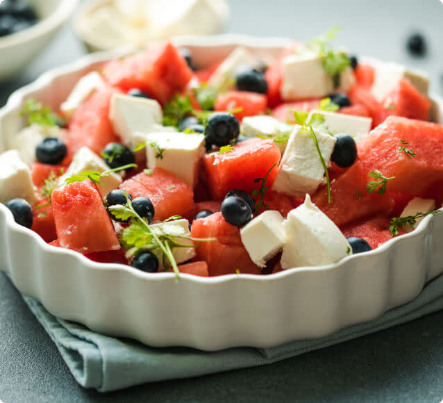 A dish full of watermelon, feta cheese, and blueberry salad garnished with fresh herbs