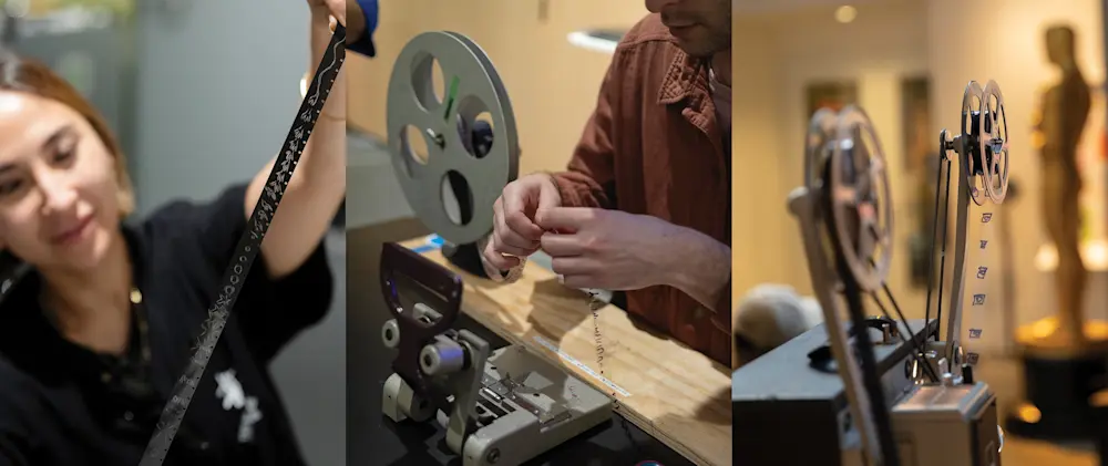 A man and woman are collaborating on repairing a film projector in a workshop setting. A man and woman are focused on fixing a film projector, surrounded by tools and equipment in a workshop.
