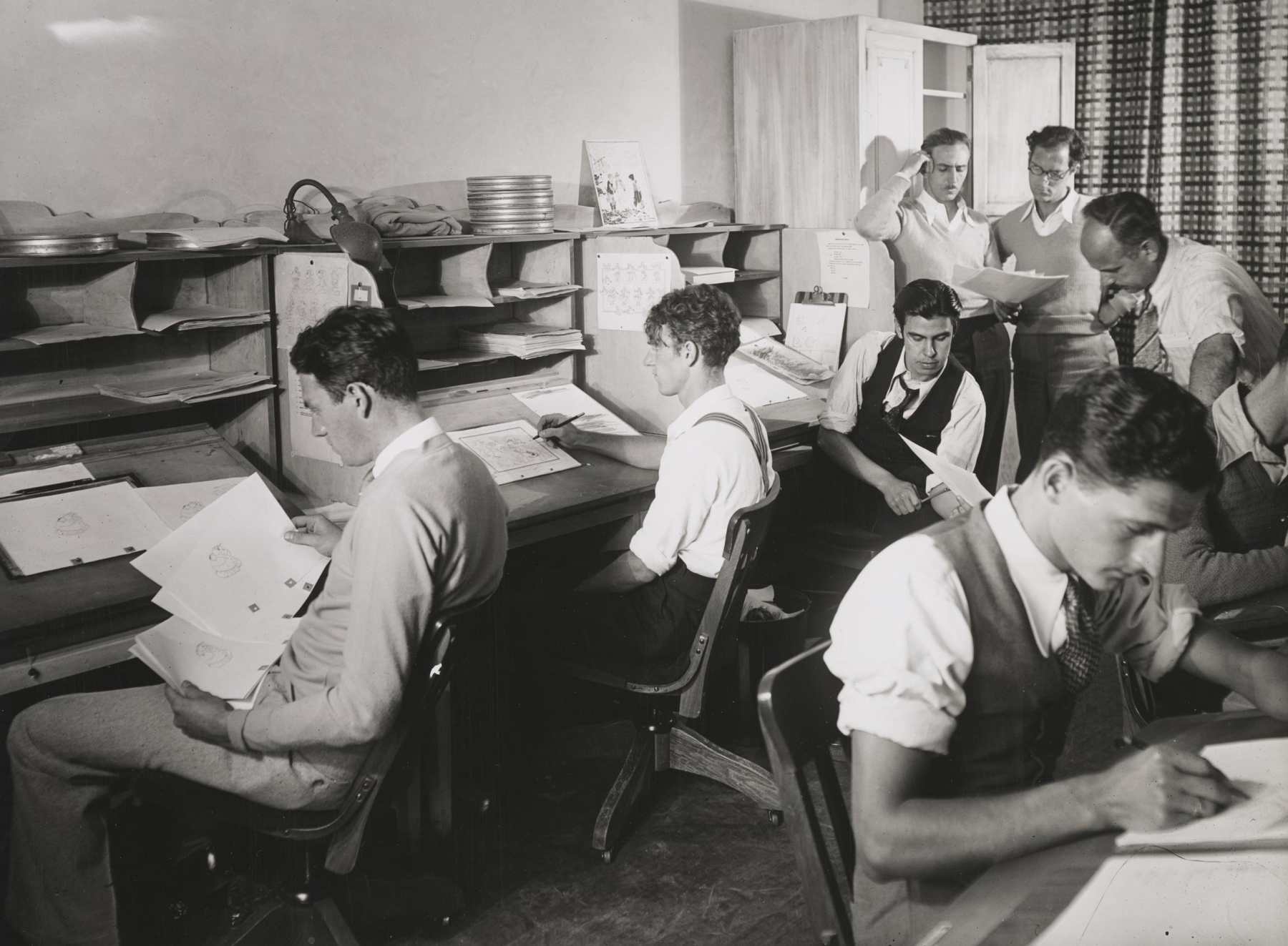 Walt Disney (standing, left) and staff (sitting, from left: David Hand, Johnny Cannon, Rudy Zamora, and Les Clark; standing middle, Tom Palmer, and standing right, Ben Sharpsteenat) at the Walt Disney Productions studio, ca. 1932, Bison Archives, photographs collected by Marc Wanamaker, courtesy of Margaret Herrick Library, Academy of Motion Picture Arts and Sciences.