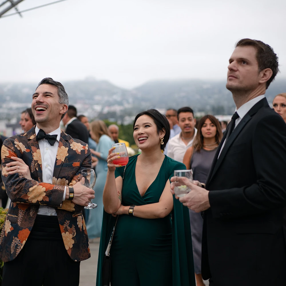 Three individuals at a party holding drinks on the Dolby Family Terrace at the Academy Museum