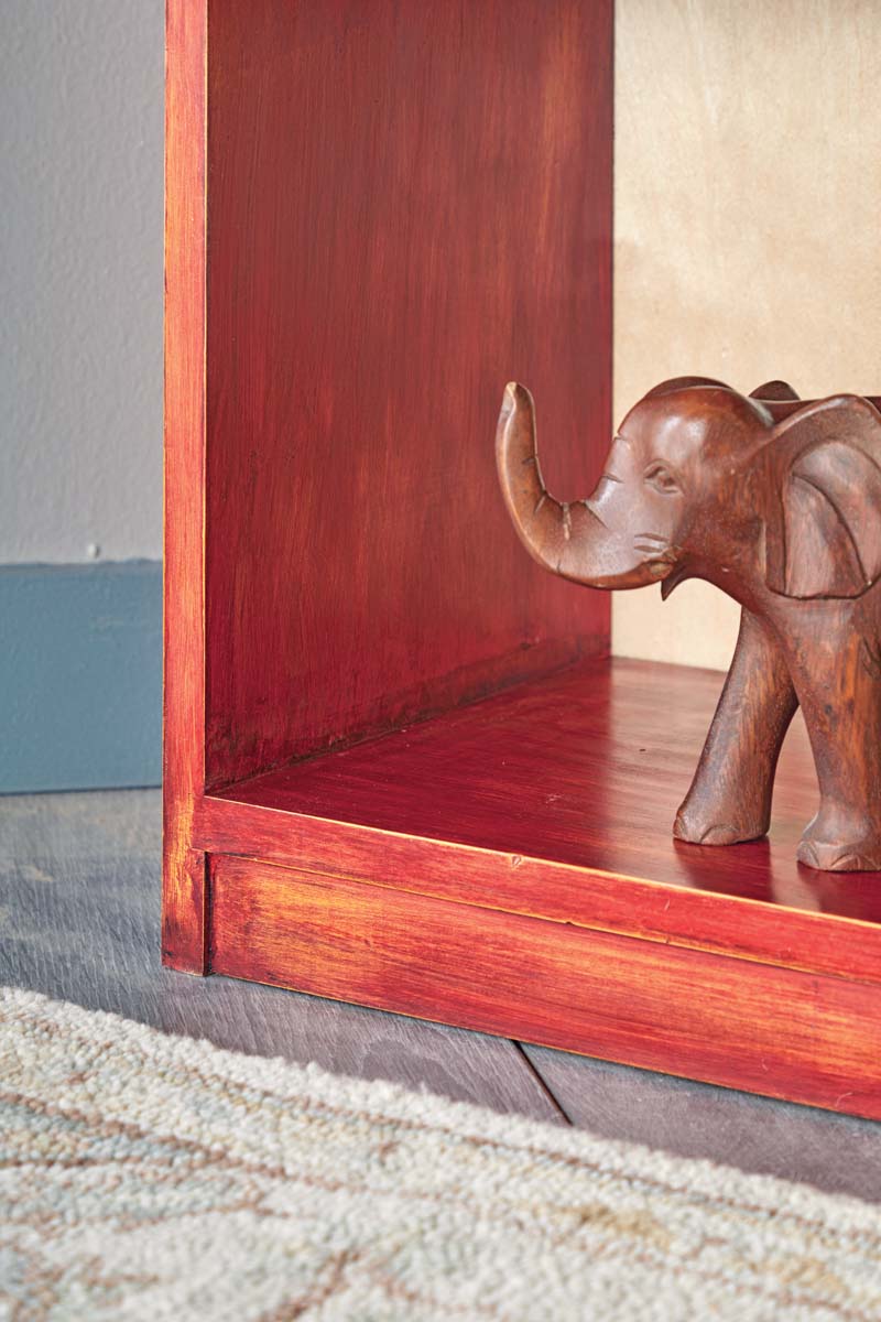 bottom of red painted pine bookcase with layered paint with yellow base showing through red top coat