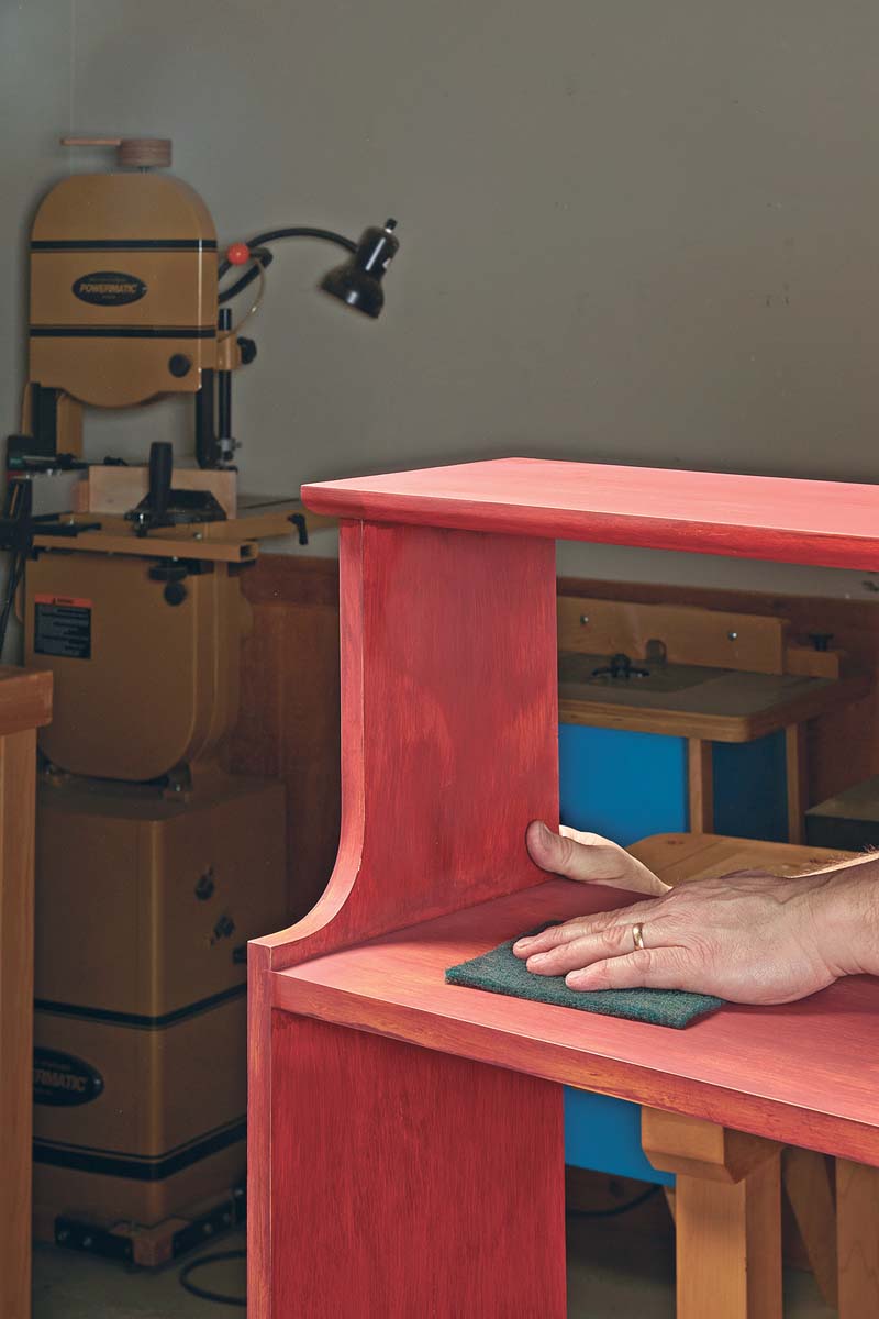 uisng abrasive pad over red painted bookshelf