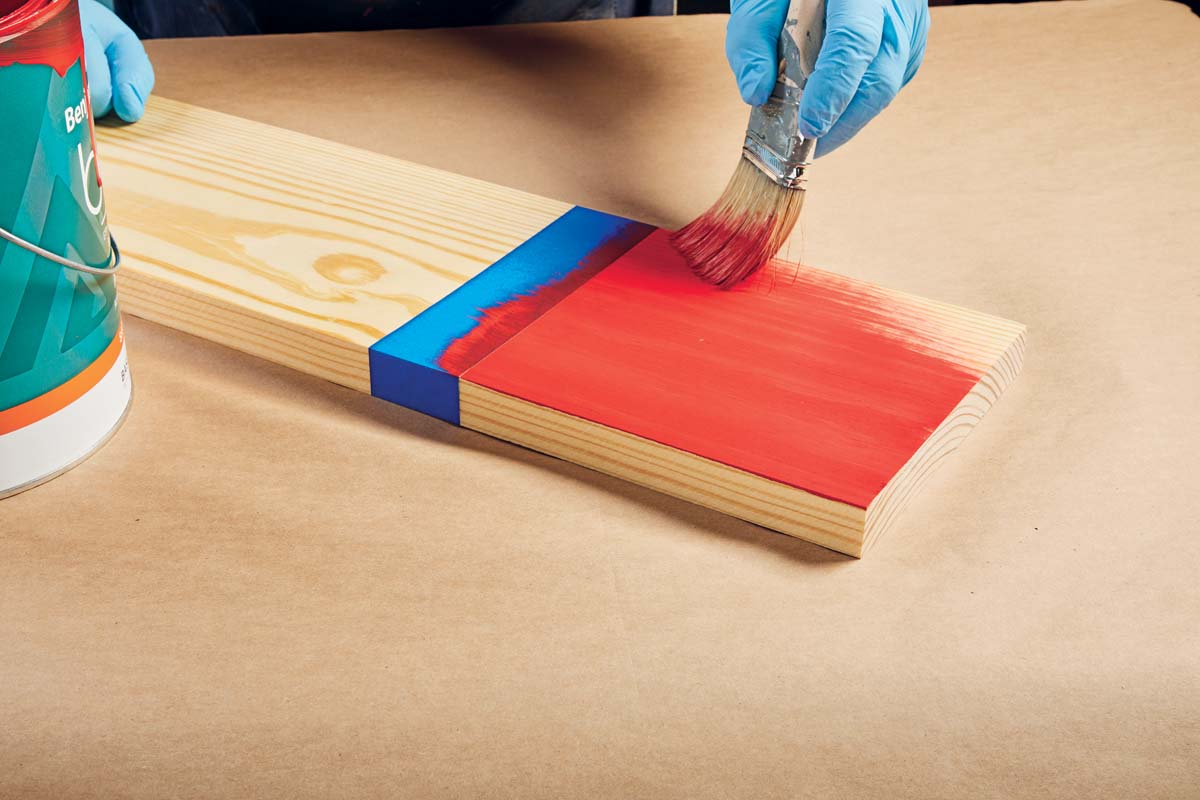 Image of wood board being painted with red paint past the line made by blue painter's tape