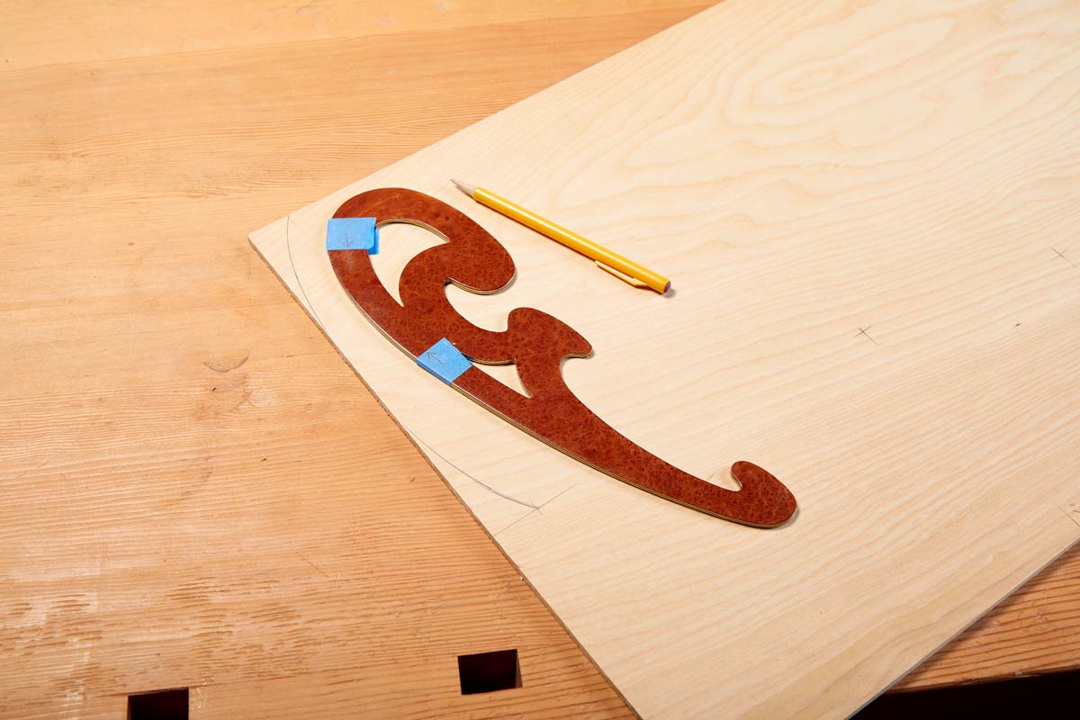 French curve template with blue masking tape markers on plywood next to yellow pencil