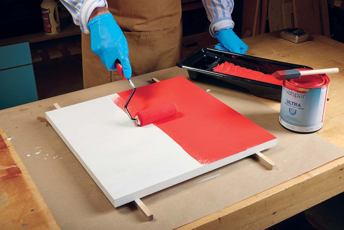 using paint roller to apply multiple coats of red high gloss paint