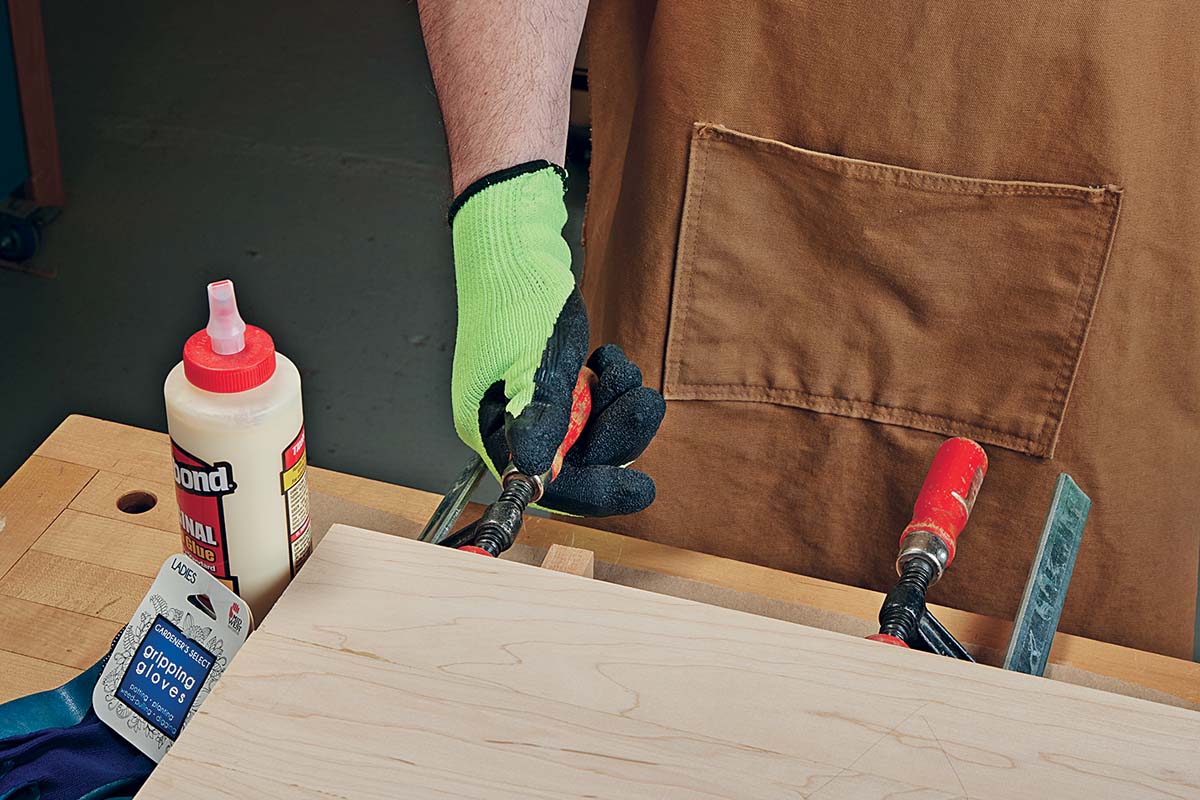 image of handing tightening clamps using rubber cloves for traction, bottle of titebound wood glue next to clamp