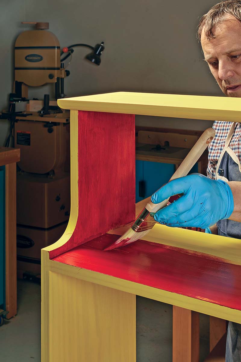 applying second coat of paint with paintbrush using red paint this time