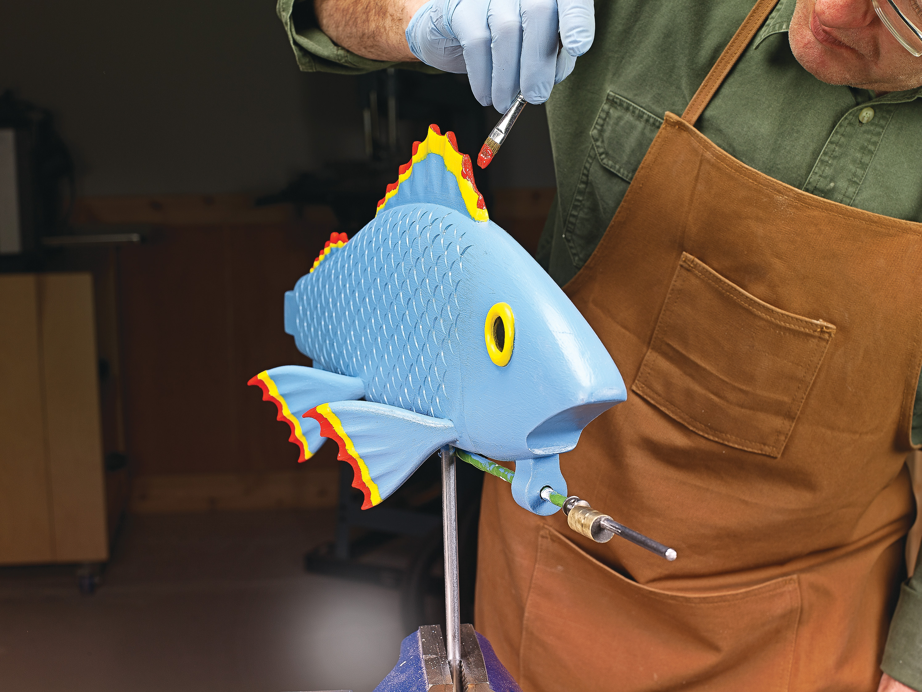 wood fish painted blue with yellow and red tipped fins, a small flat brush is used to paint red on the fin tips 
