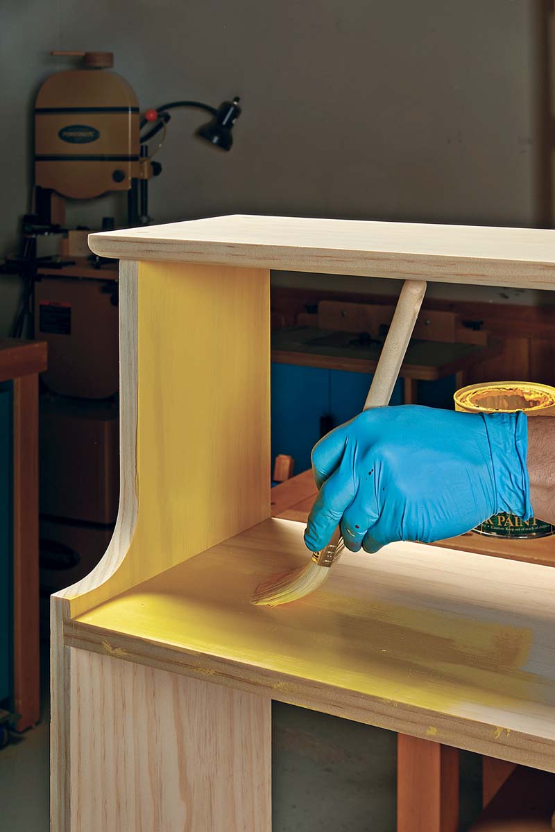 applying yellow base coat with paintbrush to pine bookshelf