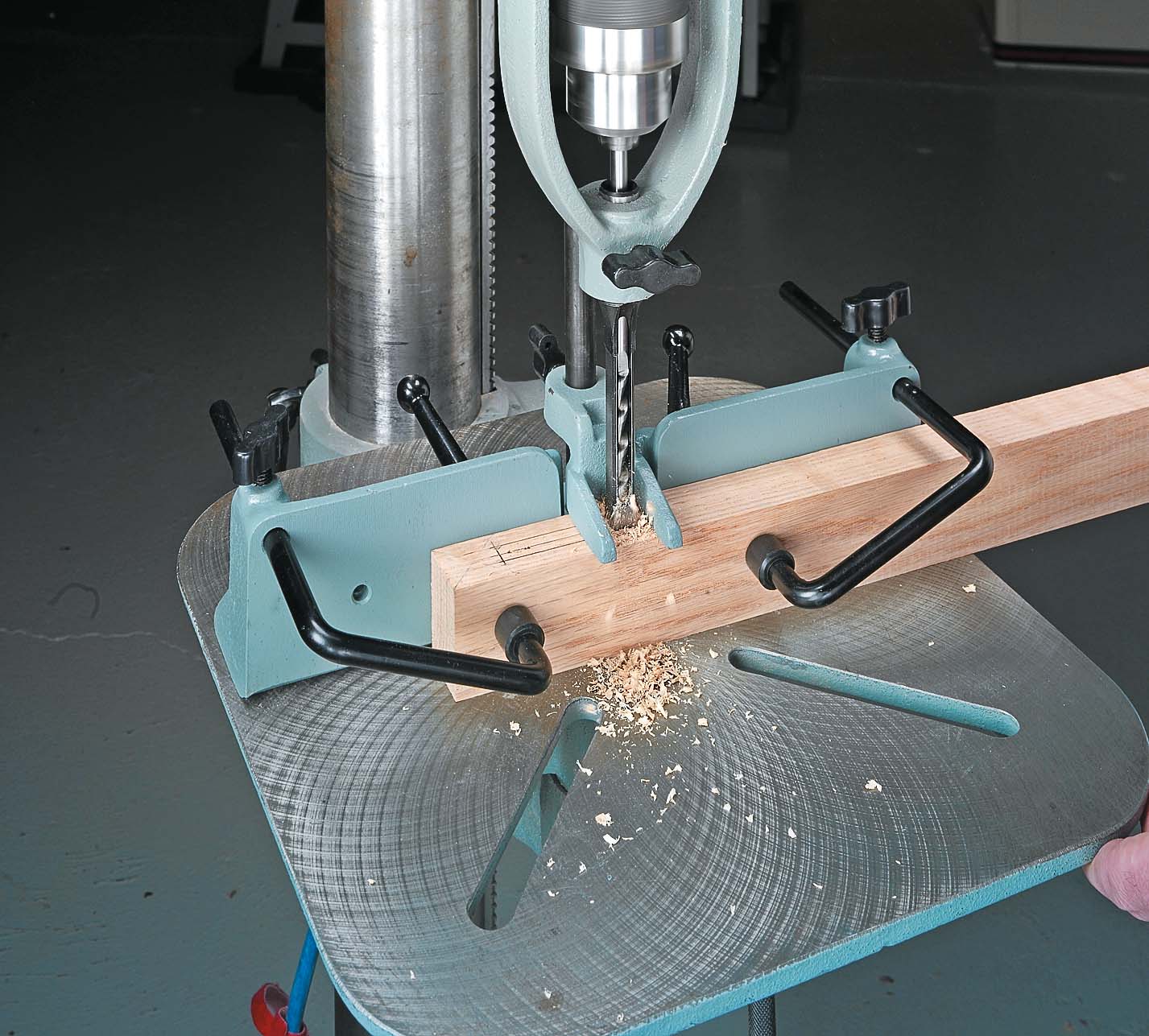 drill press with attached hollow chisel bit cutting into wood
