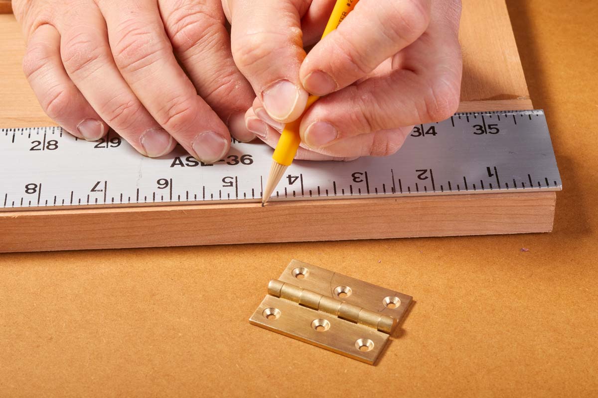 using metal ruler and pencil to mark where hinge goes