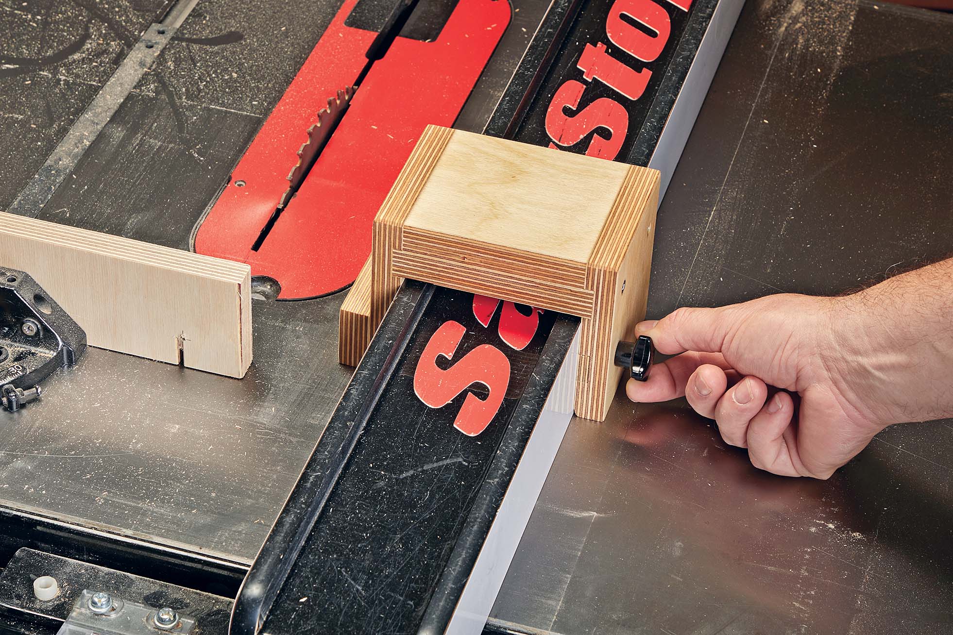 Turning the black knob on the self-clamping block over the rip fence of the table saw to clamp the block down over the fence