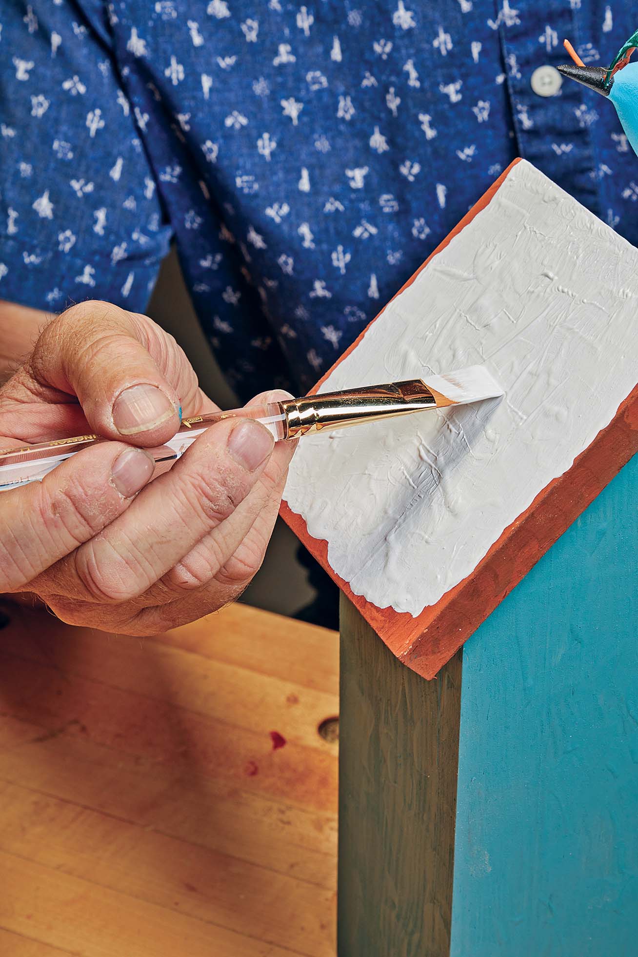 flat brush being using to paint bottom of birdhouse
