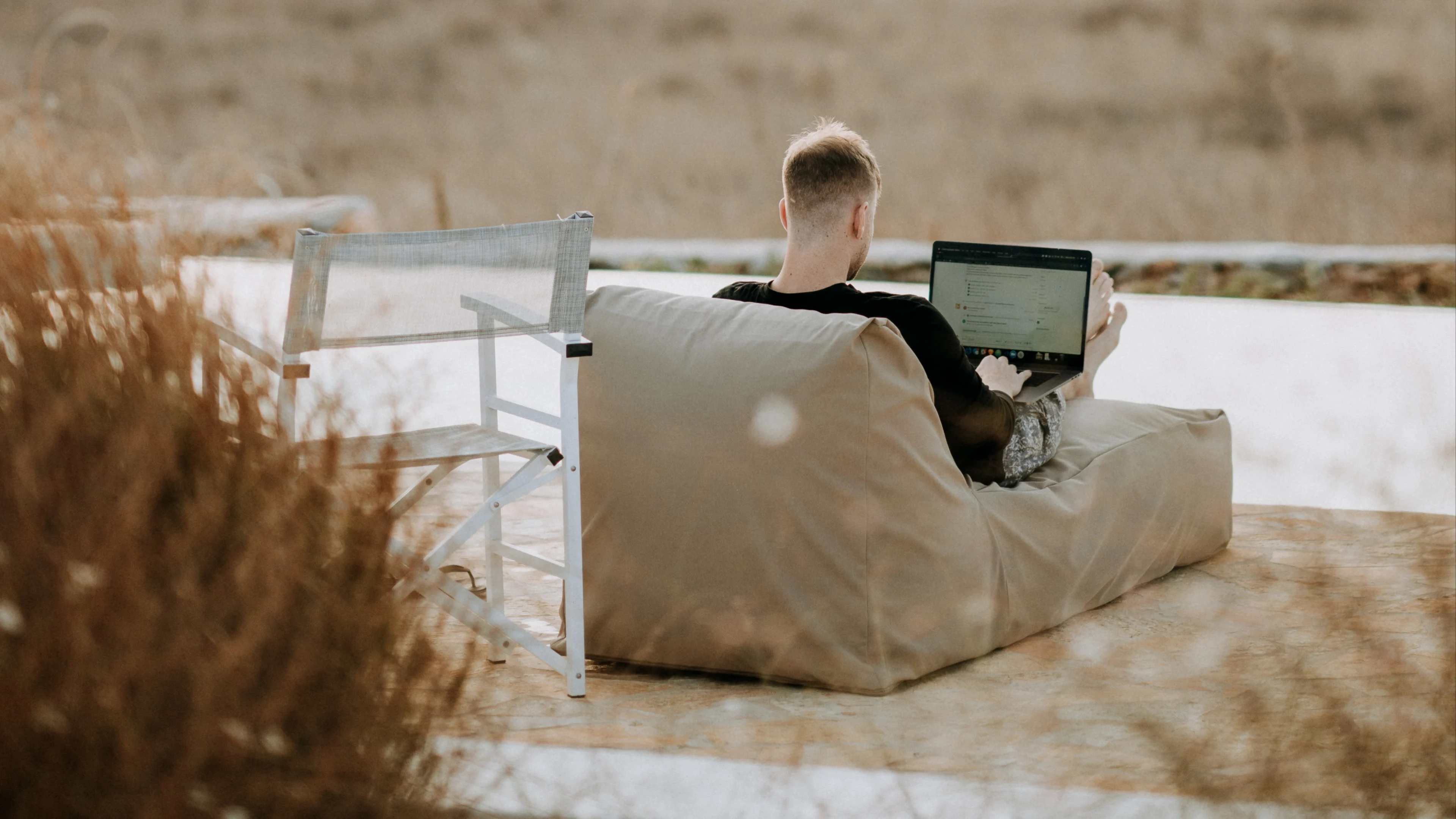 Young man from behind, sitting outside in a lounge chair with laptop 