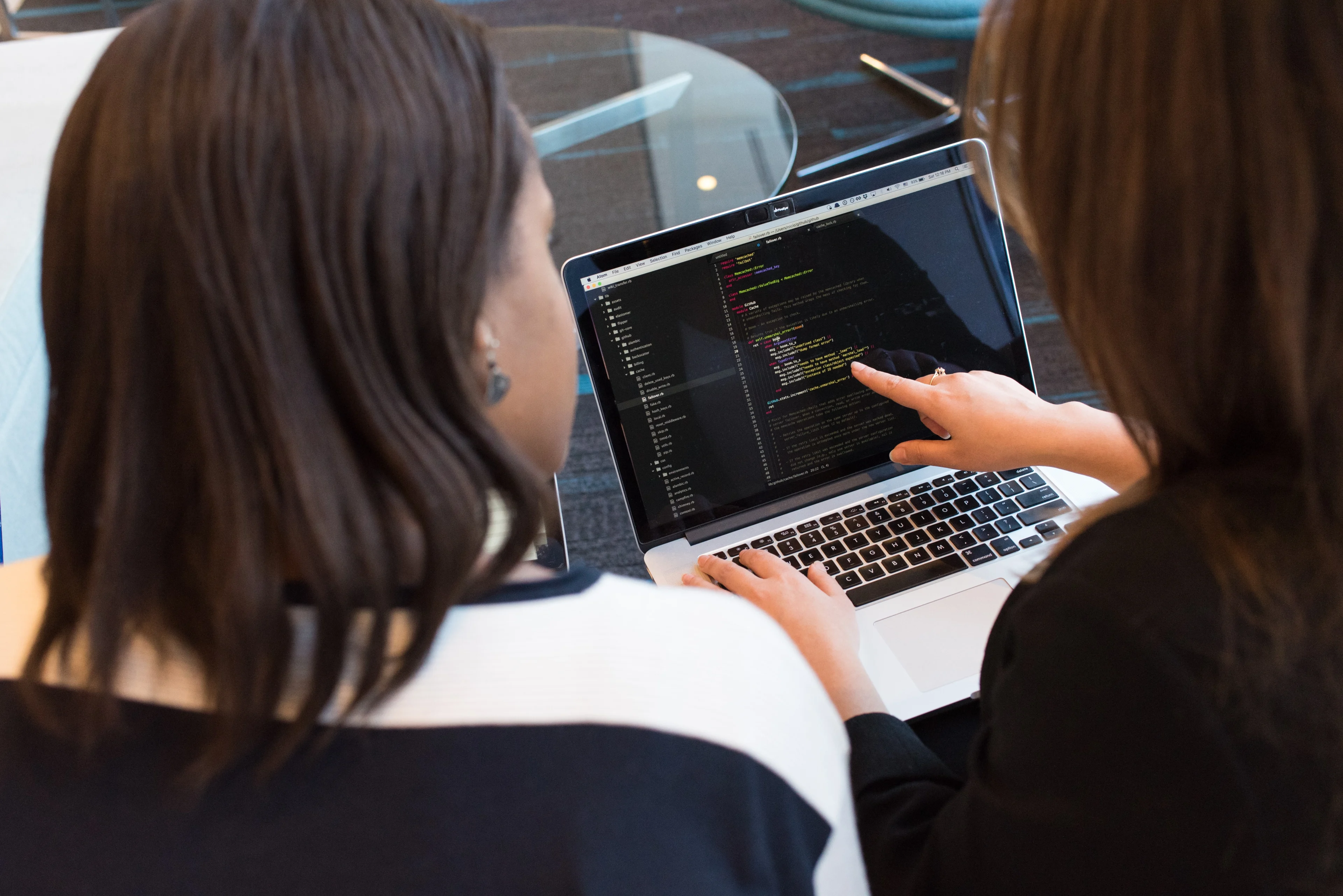 Rückenansicht zweier Frauen, die gemeinsam an einem Laptop Code besprechen.