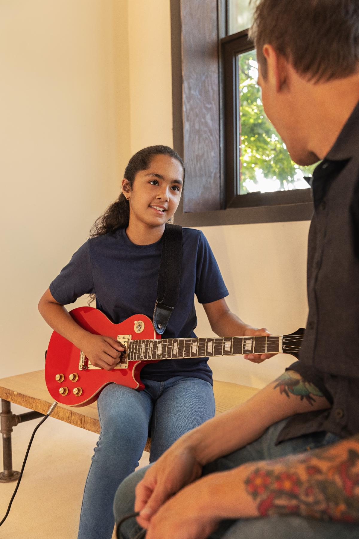 A student learns guitar on the new Epiphone Power Players Les Paul in Lava Red.