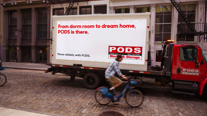 A Pods container sits on a college campus with students walking by on a cobblestone road