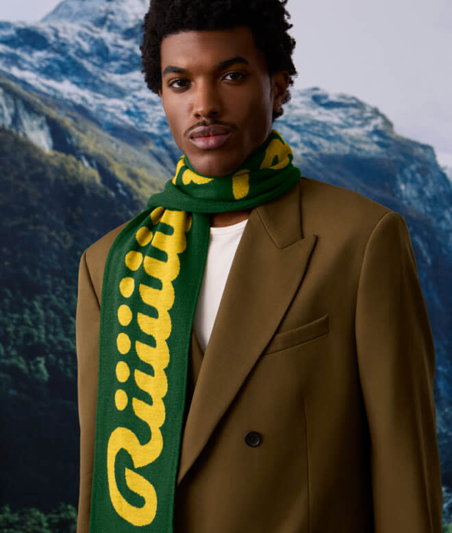 Man wearing a Ricola scarf around his neck with mountains in the background